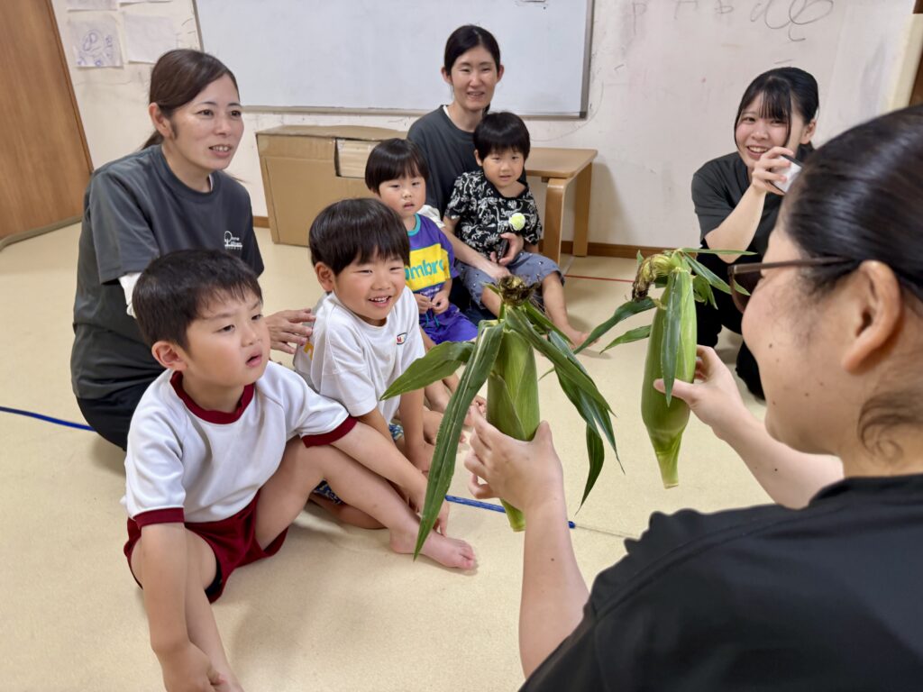 皮付きのトウモロコシを見て笑顔になるこども