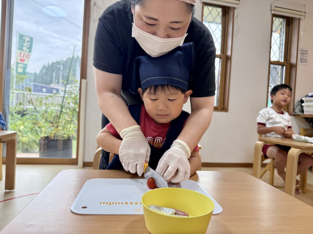 鹿児島市・日置市からこどもたちが通う児童発達支援事業所(療育支援事業所)アナベルキッズで、 スタッフに手を添えてもらいながら包丁で食材を切る様子