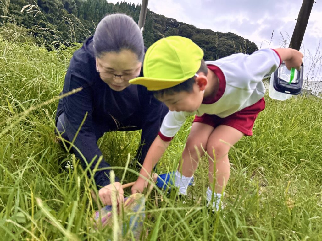 鹿児島市の児童発達支援アナベルキッズで、スタッフと草むらをのぞいて虫を探すこども