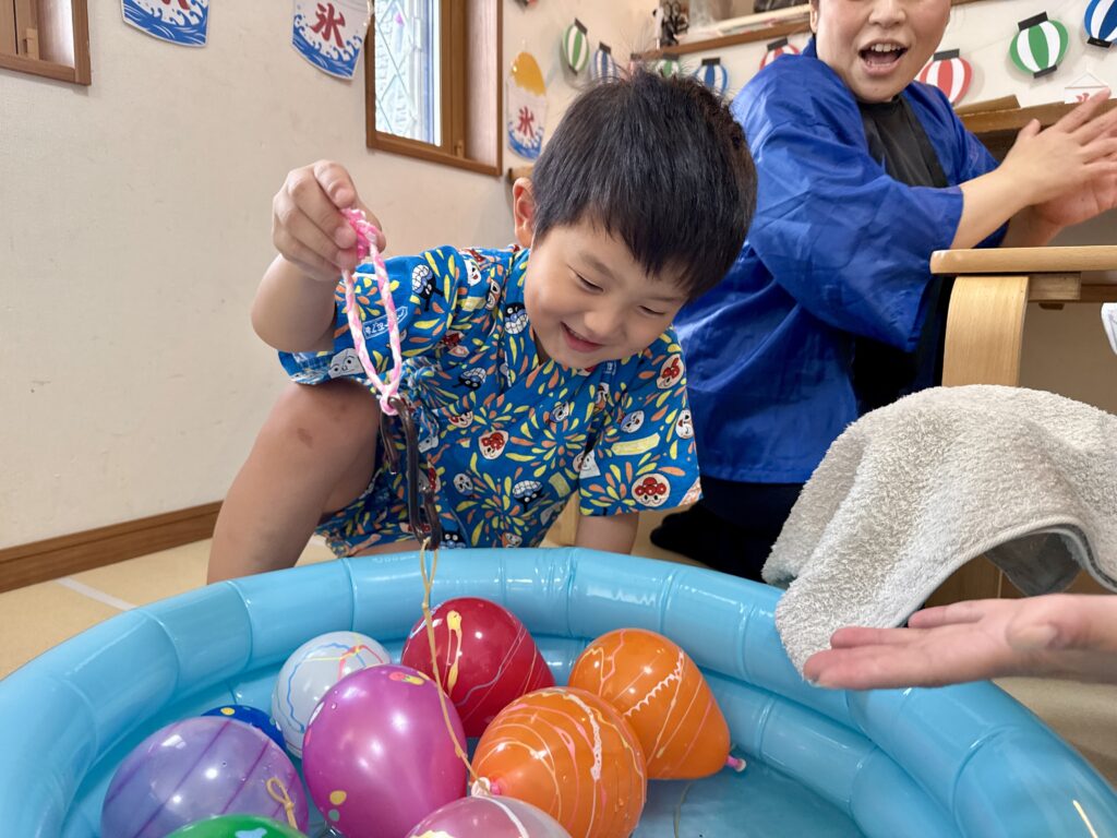 青い水槽の水ヨーヨーに釣り針を近づける甚平姿の子どもと隣にいる青い法被姿の大人