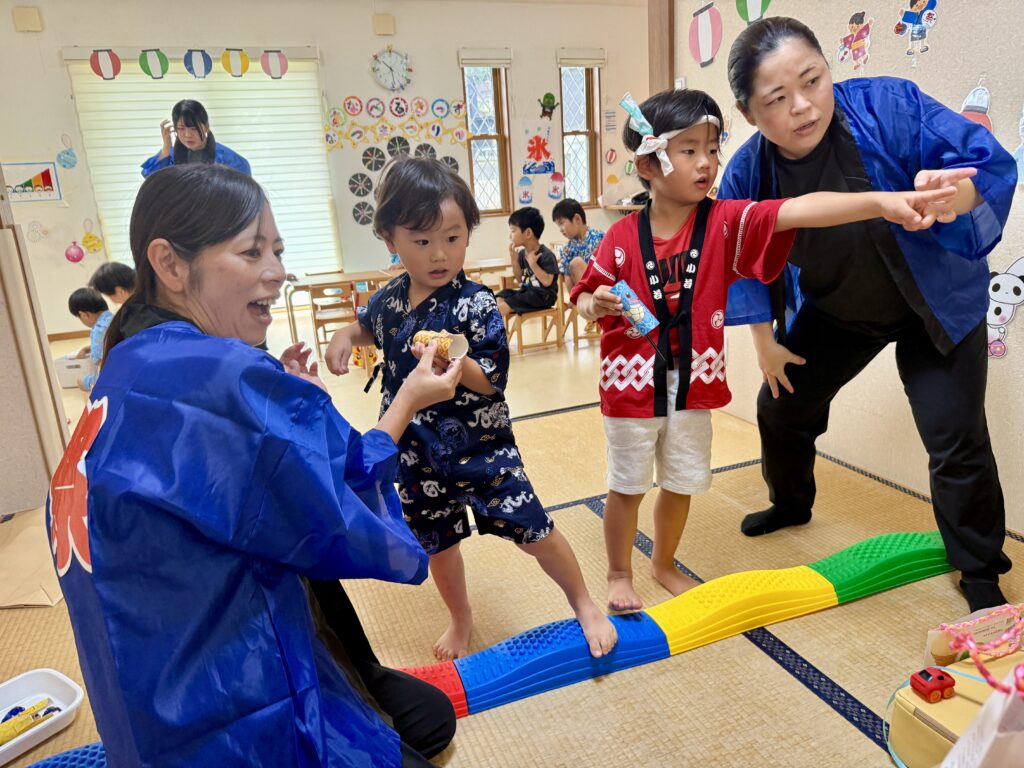 青い法被姿の大人のそばで、カラフルな細長い遊具を渡る甚平姿の子ども