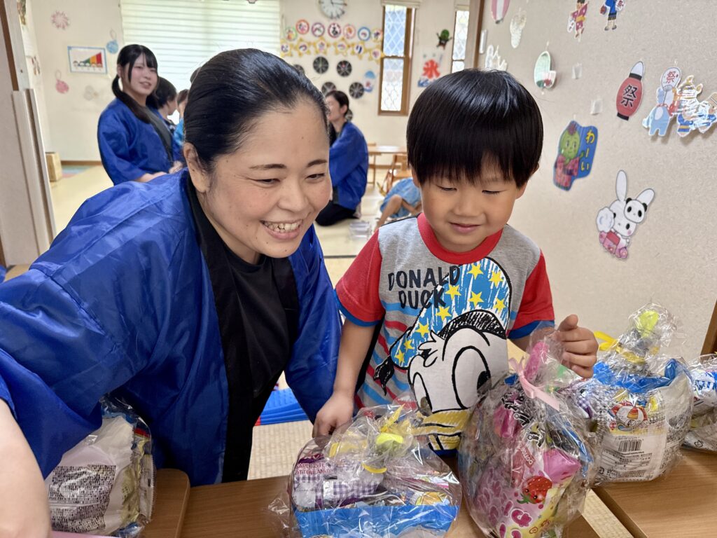 青い法被姿の大人と一緒に、透明な袋に入った品物を見る子ども