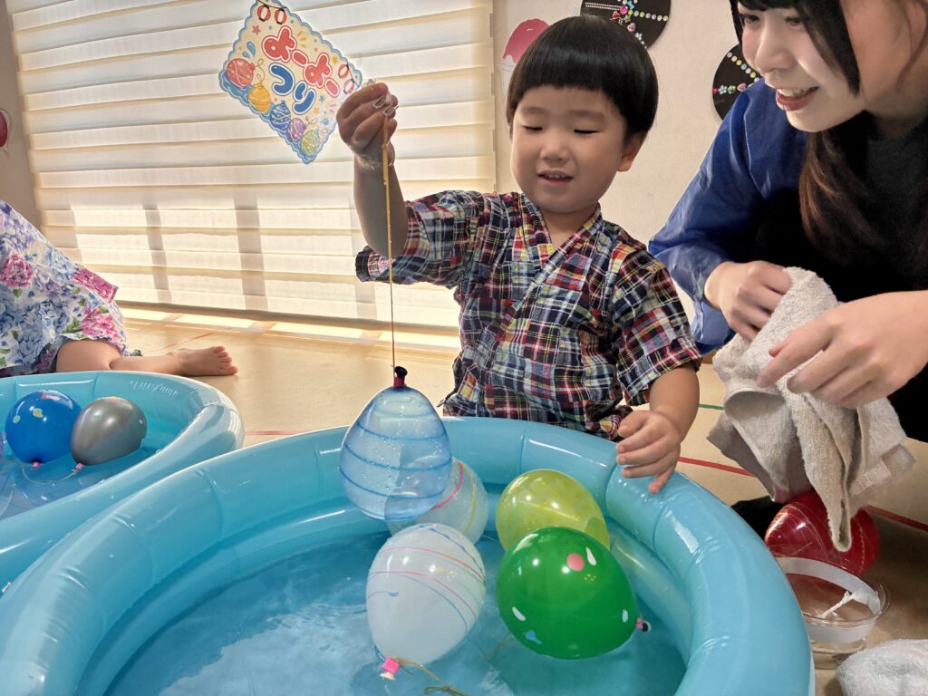 青い水槽から水ヨーヨーをつり上げる浴衣姿の子どもと隣にいる青い法被姿の大人