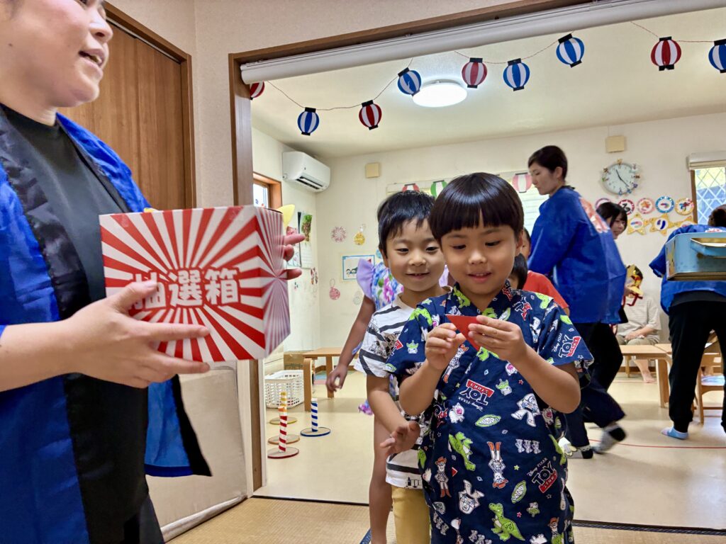 抽選箱の前で赤いくじを開く甚平姿のこども