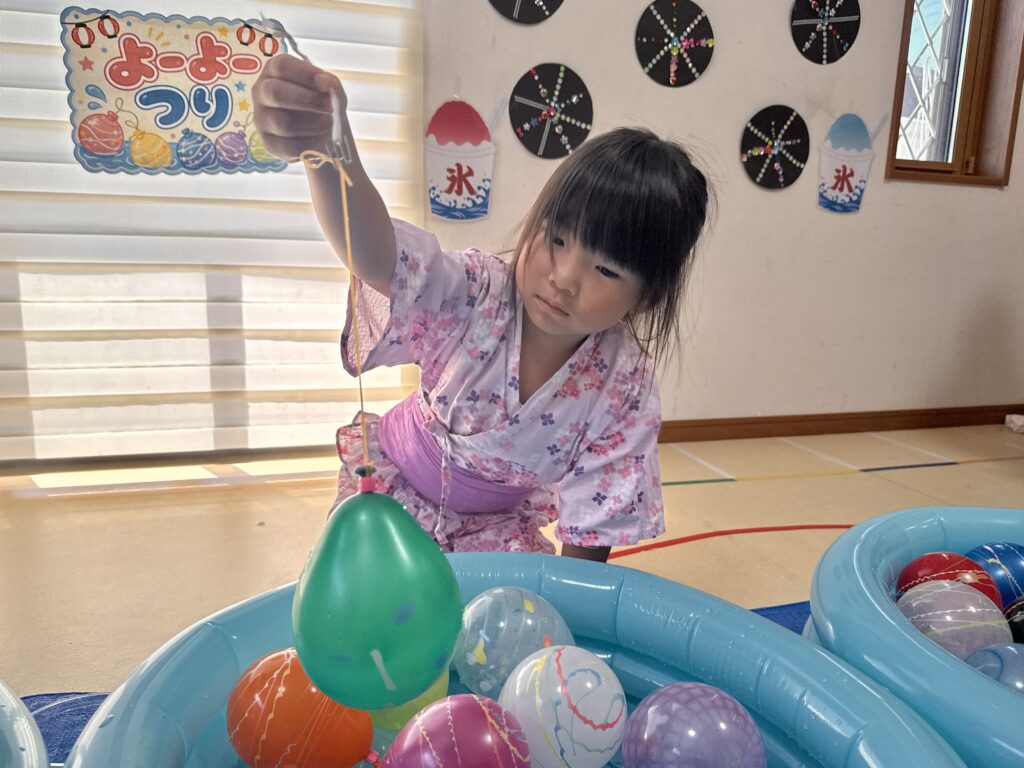 緑色の水ヨーヨーを持ち上げるピンクの浴衣姿のこども