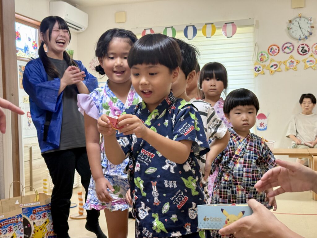 赤いくじを手に景品の箱の前に立つ甚平姿のこども