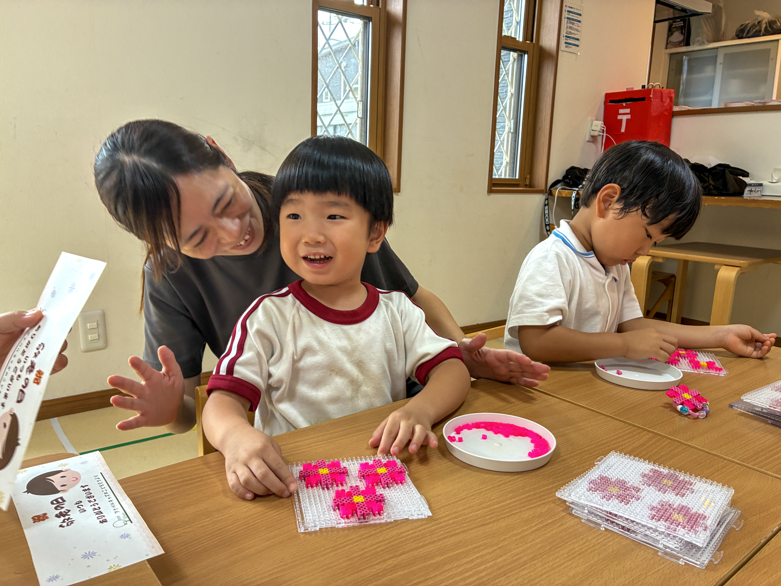 敬老の日のプレゼント作りで、花形のビーズを前に笑顔を見せる子どもと職員