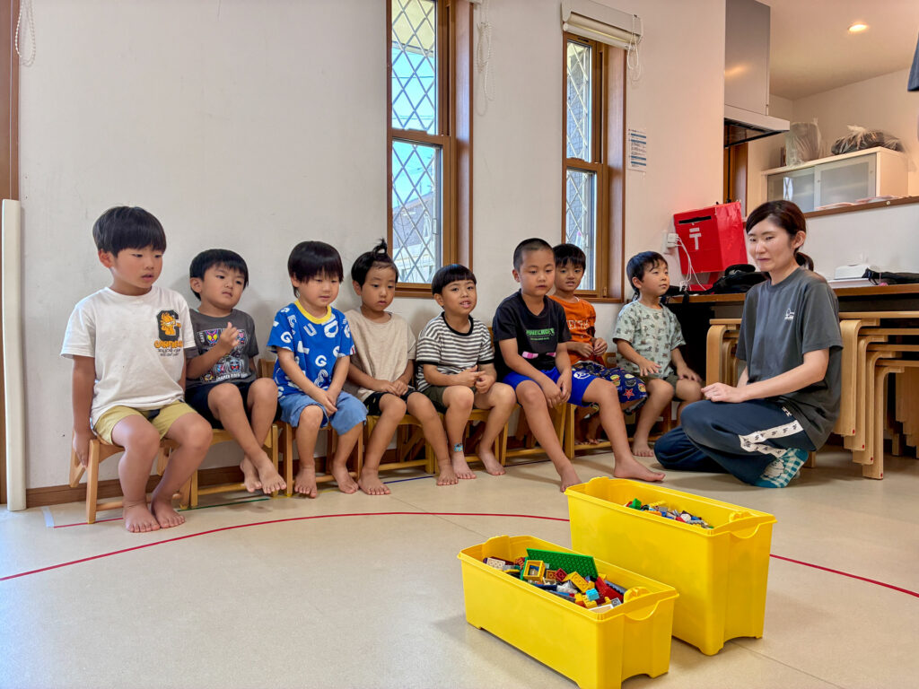 ブロックの箱を前に、こどもたちとスタッフが集まる場面