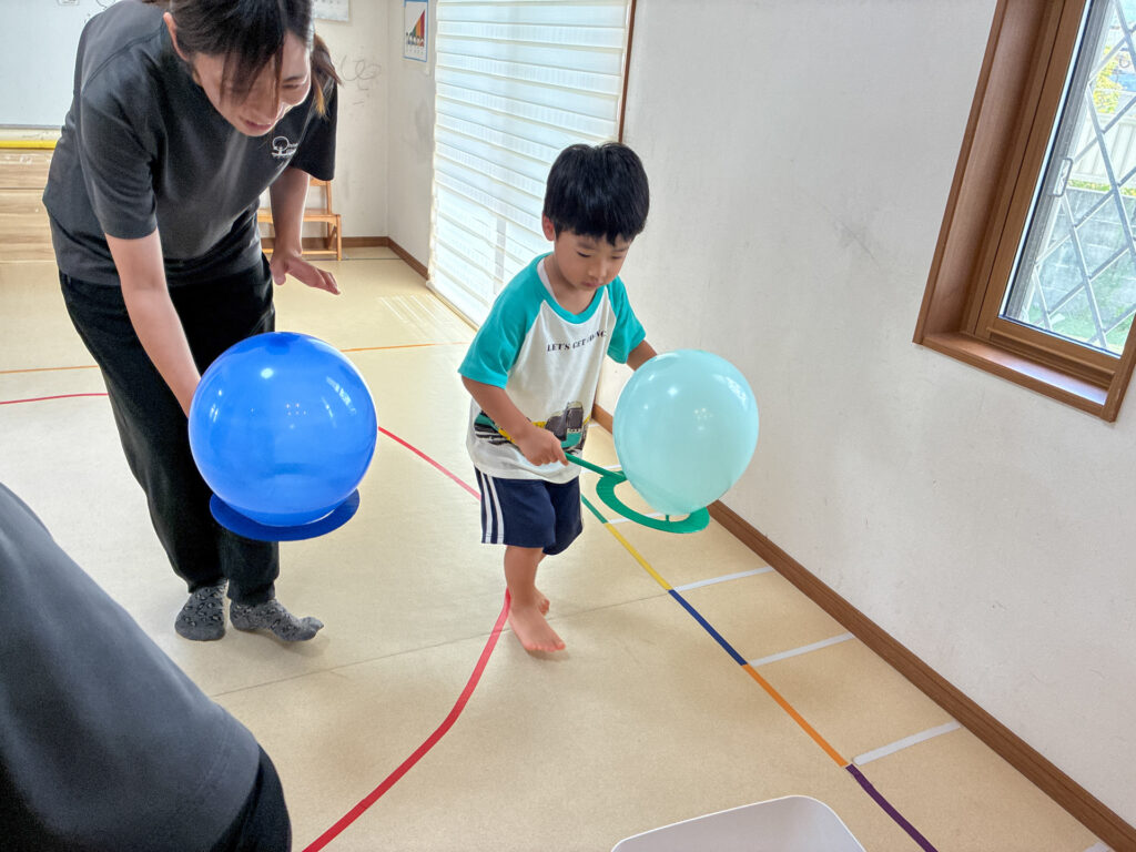 スタッフのそばで輪と風船を持って遊ぶ様子
