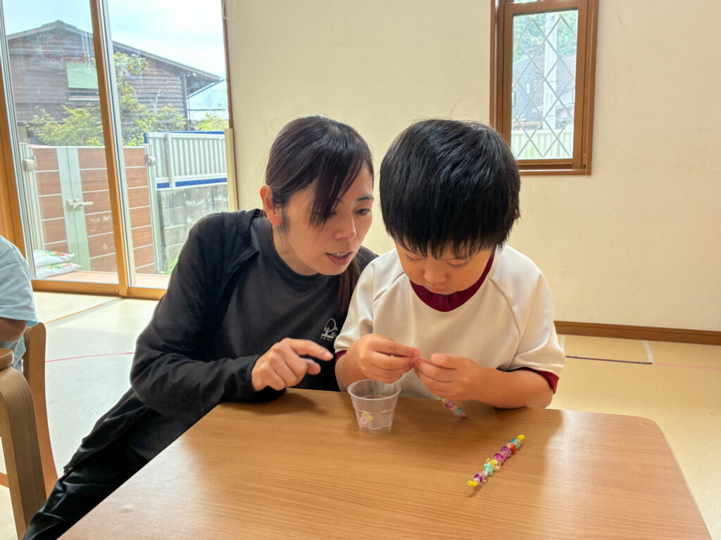 スタッフと手元を見ながらビーズを通す様子