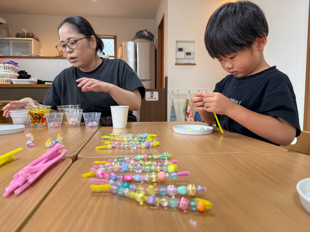 色とりどりの飾りが並ぶ机でビーズを通す様子