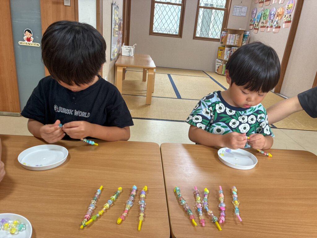 ビーズの飾りが何本も並んだ机で作る様子