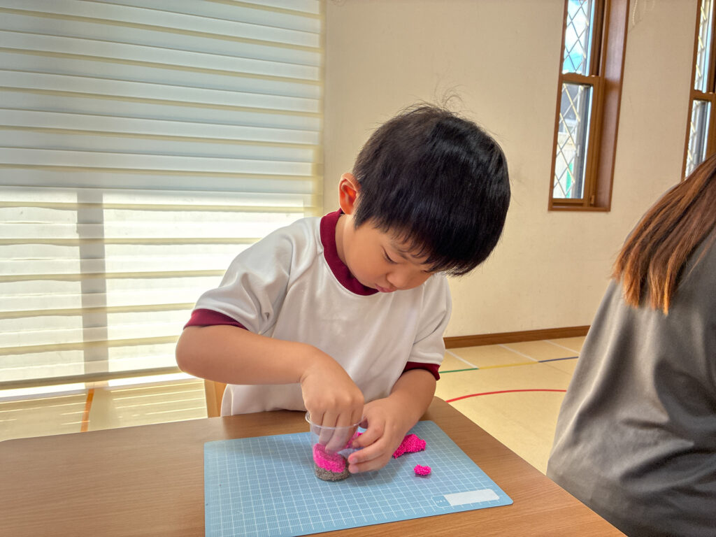 ピンクの粘土を指で押してカップに入れる様子