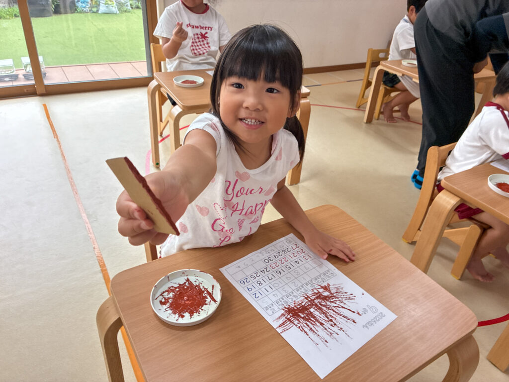 絵の具を付けた段ボールの道具を見せる笑顔