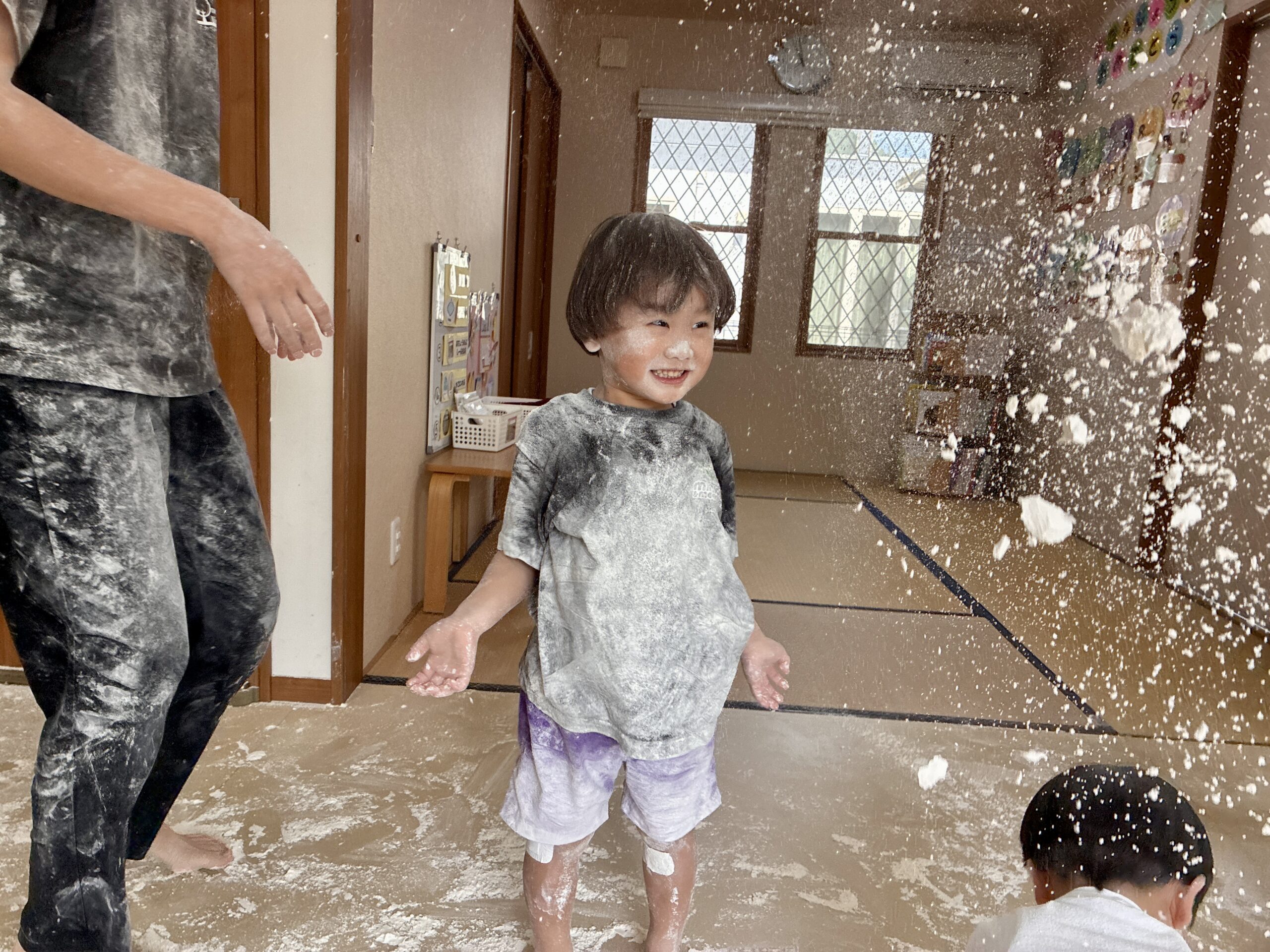 舞い上がる小麦粉の中で笑う子とスタッフ