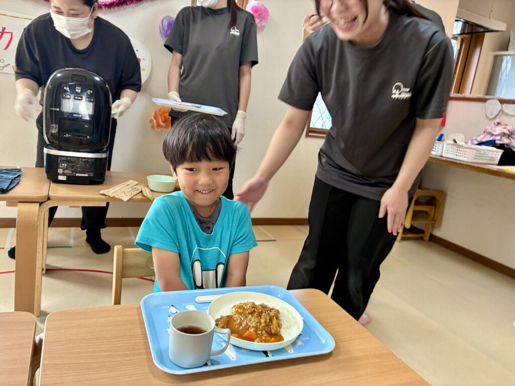 カレーライスをのせたトレーの前で笑顔のこども