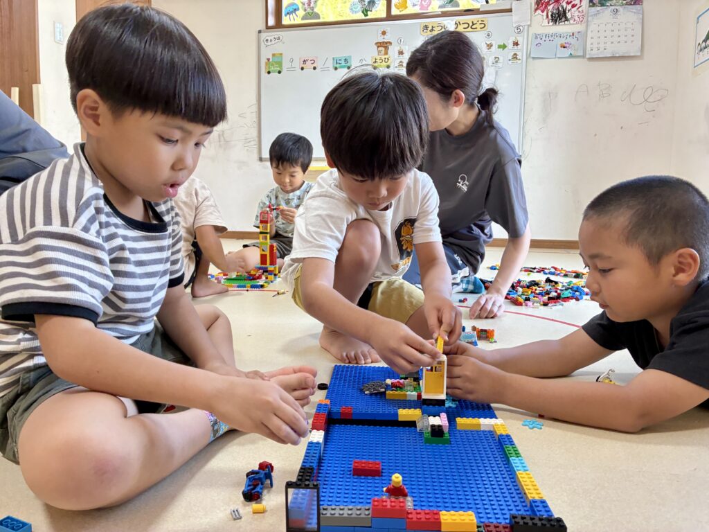 連なったブロックの板を囲んで一緒に作る数人