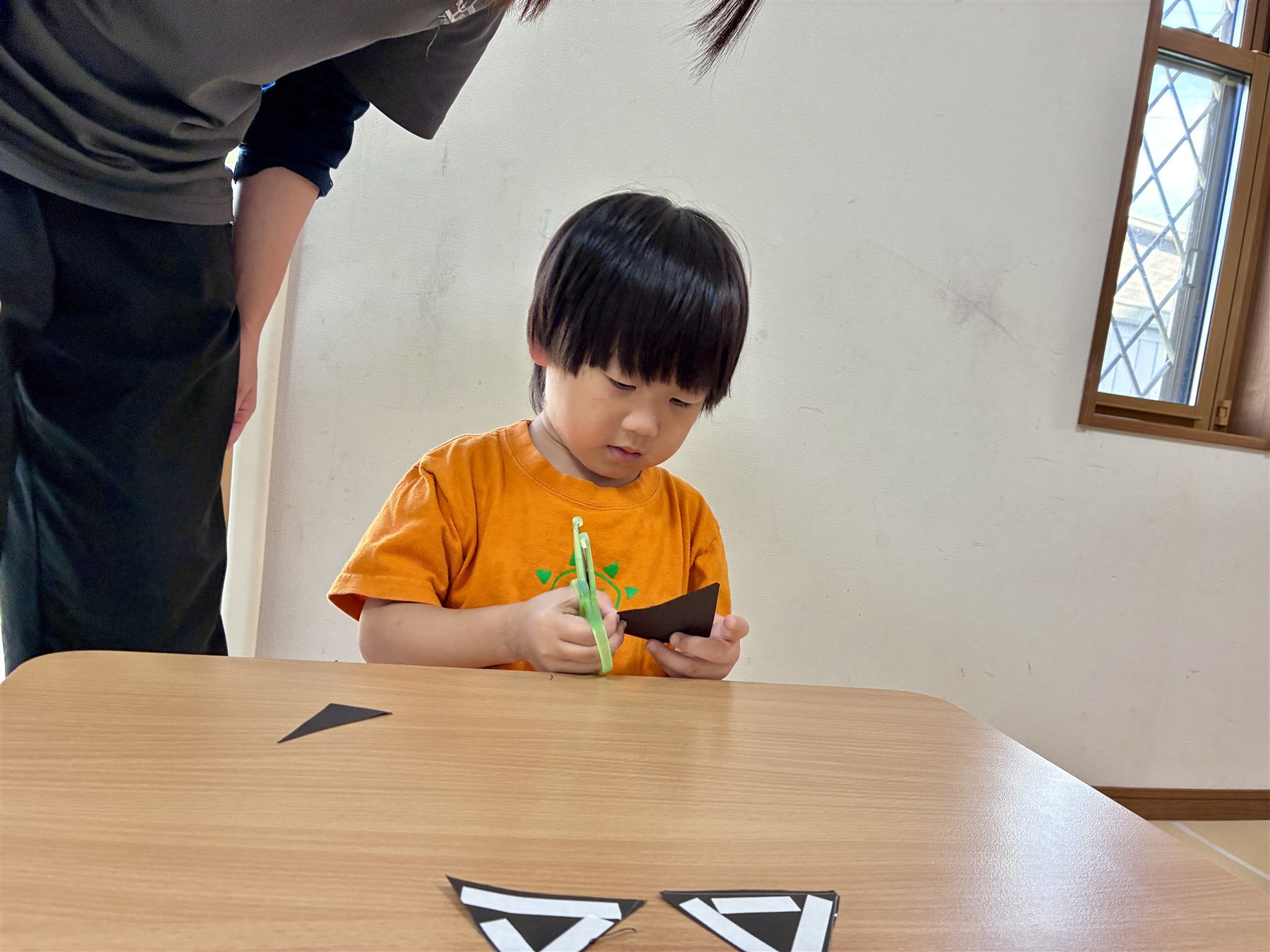 ハサミで黒い紙を切るこども。机には、切り出した三角