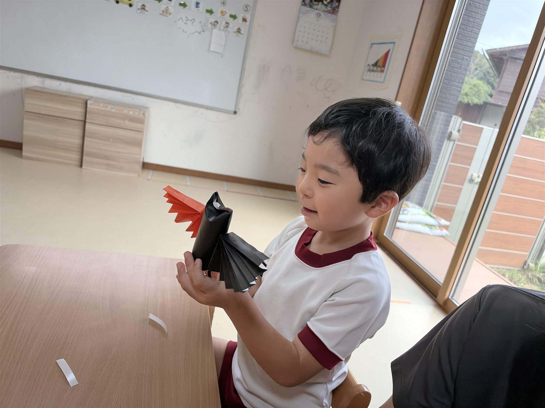 黒い折り紙とオレンジの羽根のコウモリを見つめるこども