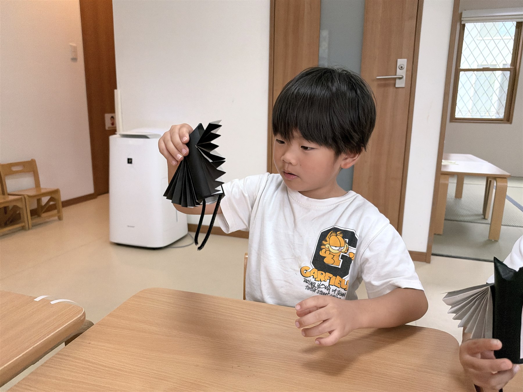 じゃばら折りの黒い羽根のコウモリを持ち上げて見つめるこども