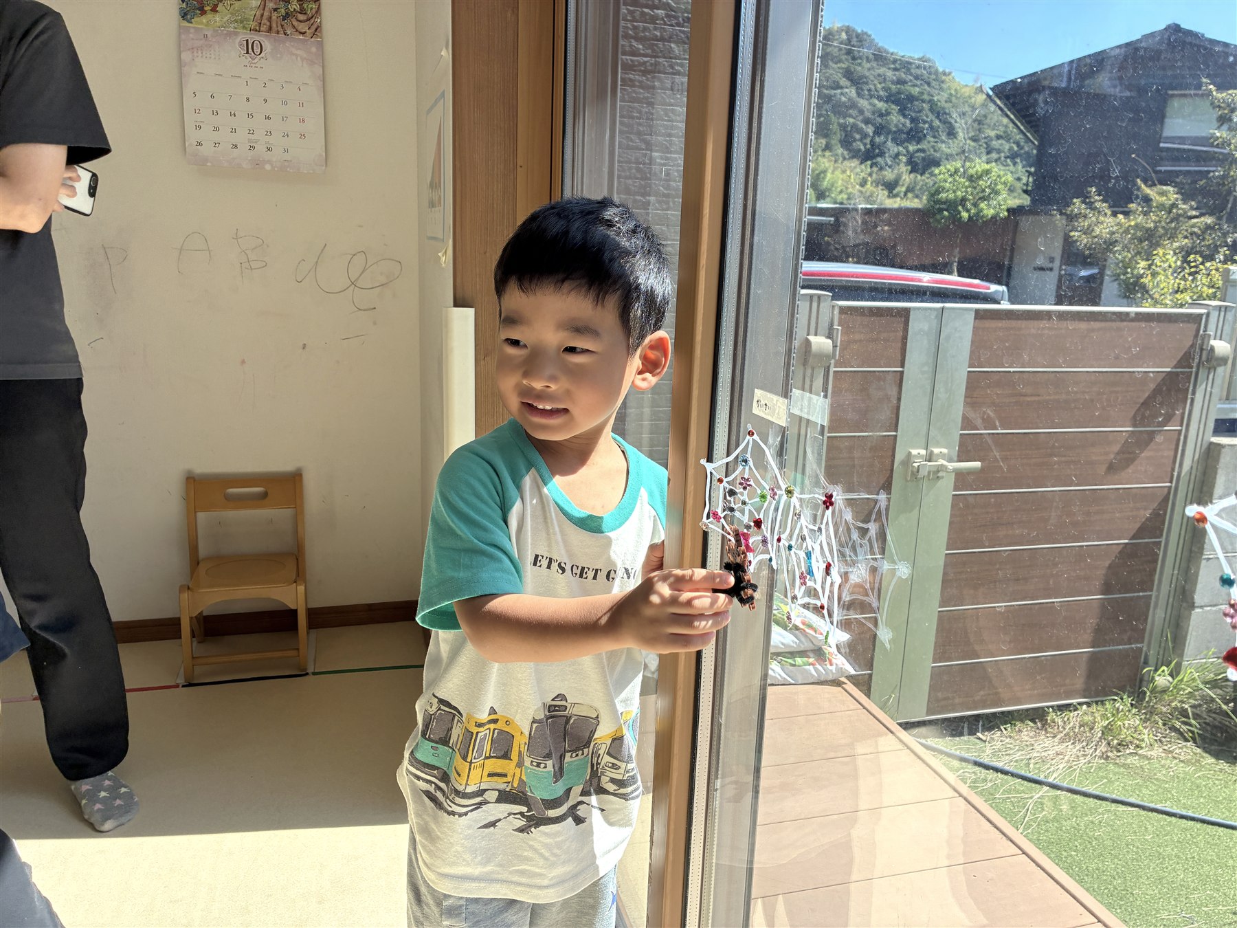 窓ガラスに飾った蜘蛛の巣に手を添えるこども
