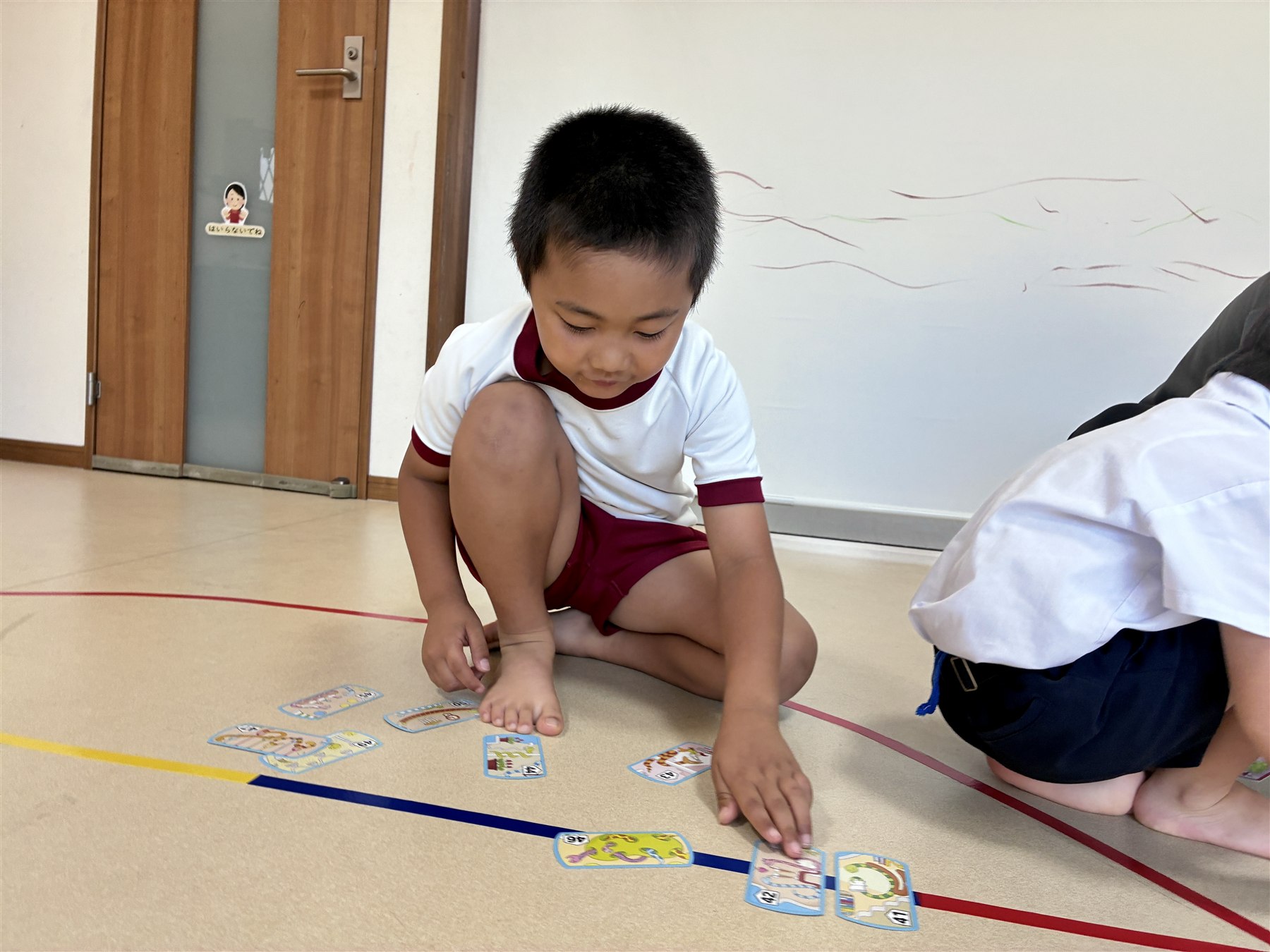 床にしゃがんで、数字のカードを並べるこども