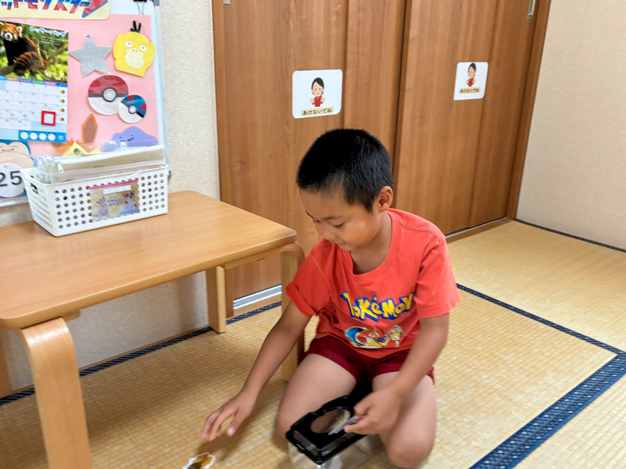 畳の上で虫かごを持ち、虫のカードに手を伸ばす子ども
